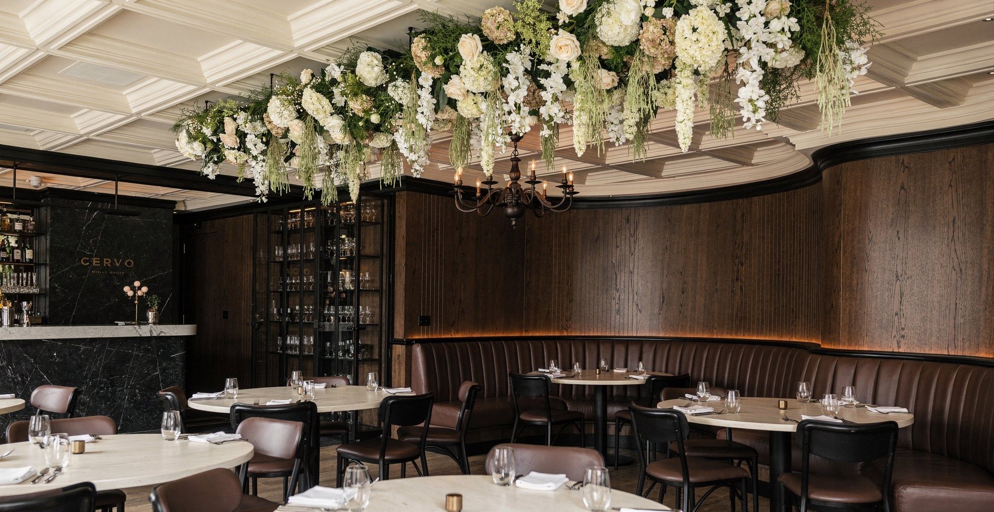 Dining room of a restaurant rebranded by Vertical Ignition — dark oak panelling, leather banquettes and a suspended floral installation
